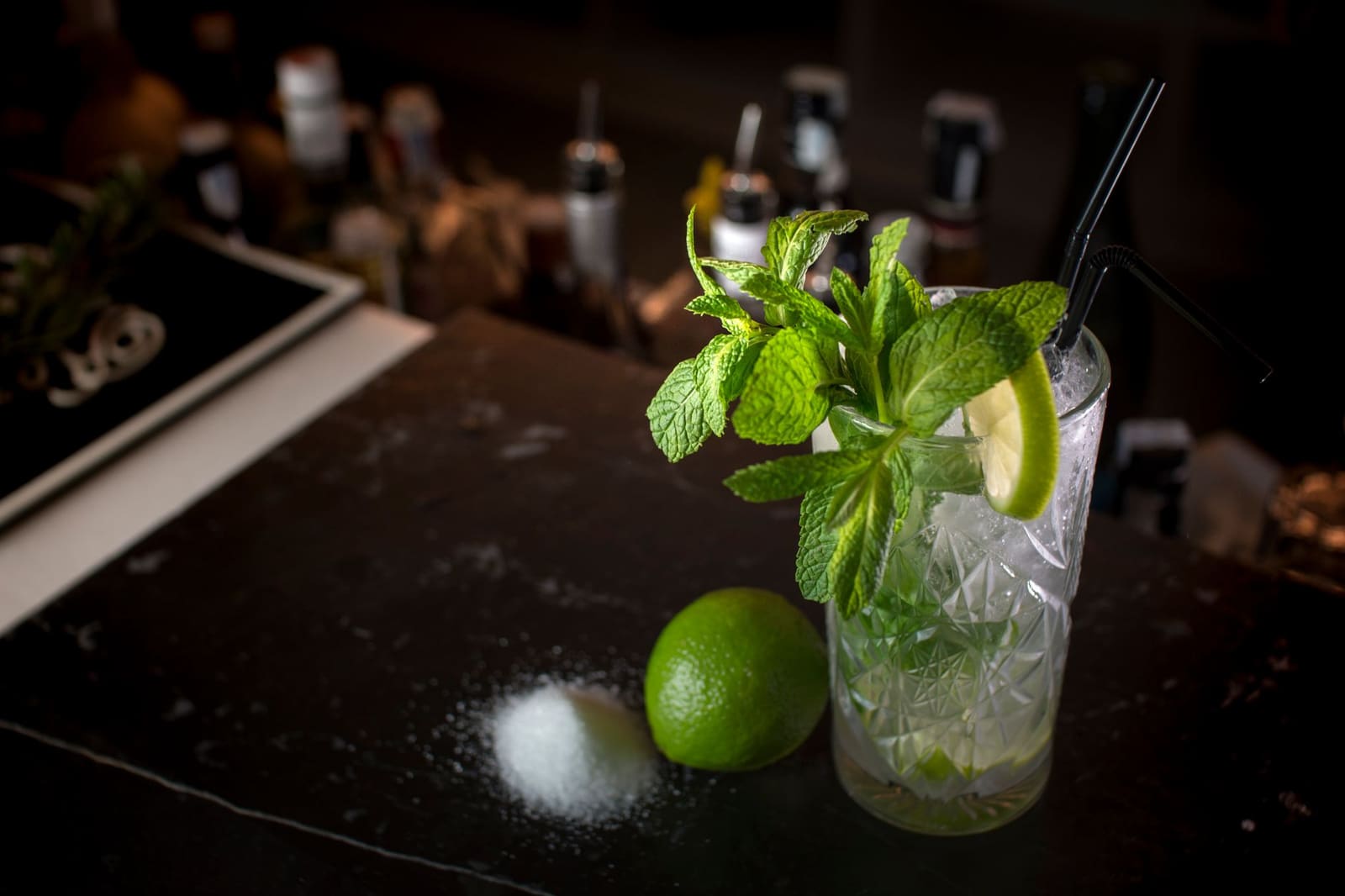 Glas mojito met munt, limoen en rietjes op donkere bar.