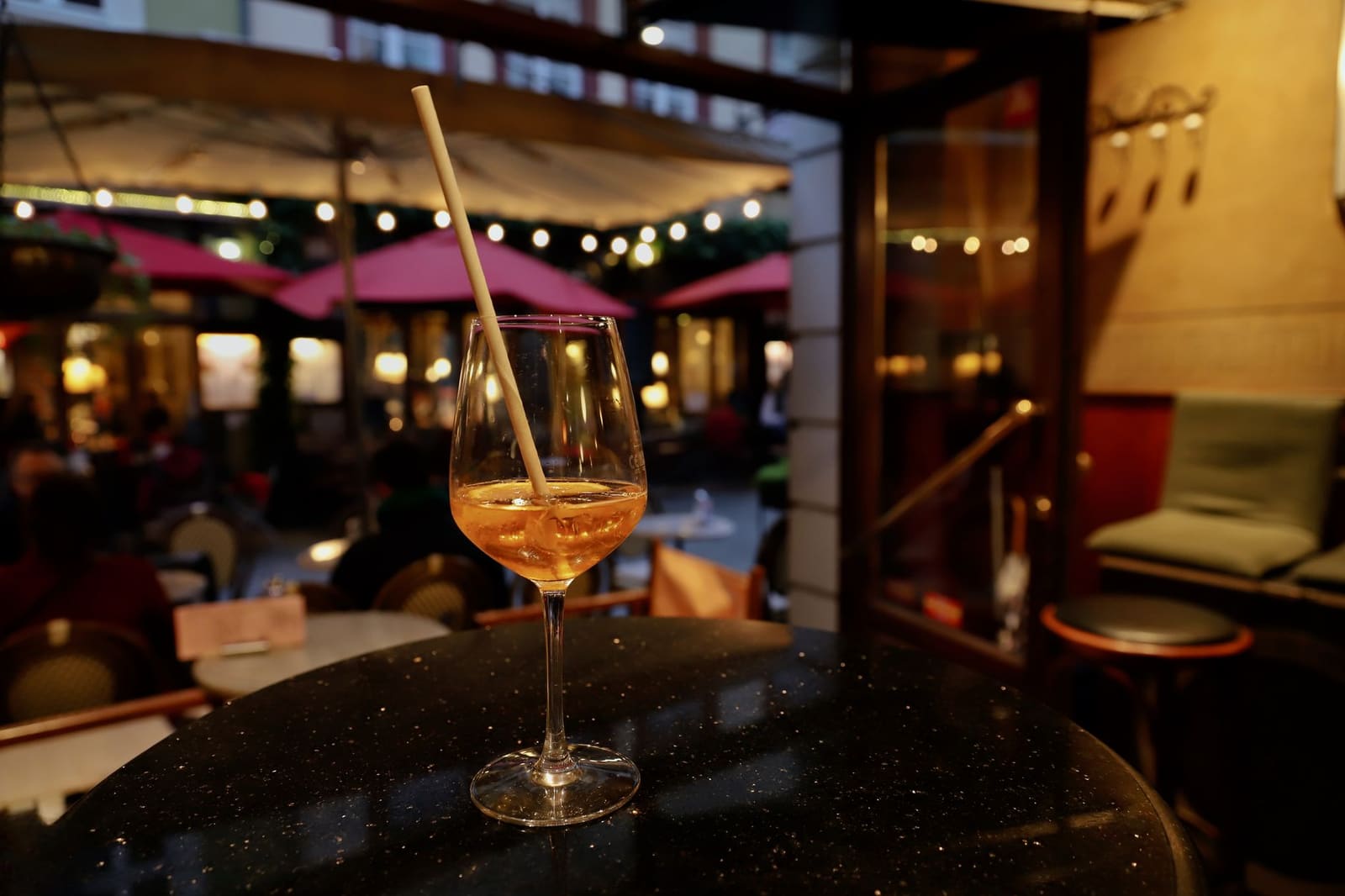 Een aperol spritz met rietje staat op een tafel op een verlicht terras.