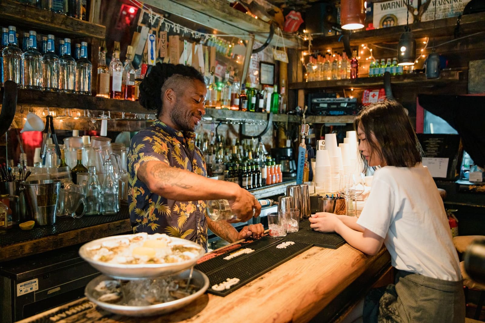 Een bartender schenkt een drankje in een glas terwijl een gast glimlacht aan de toog.