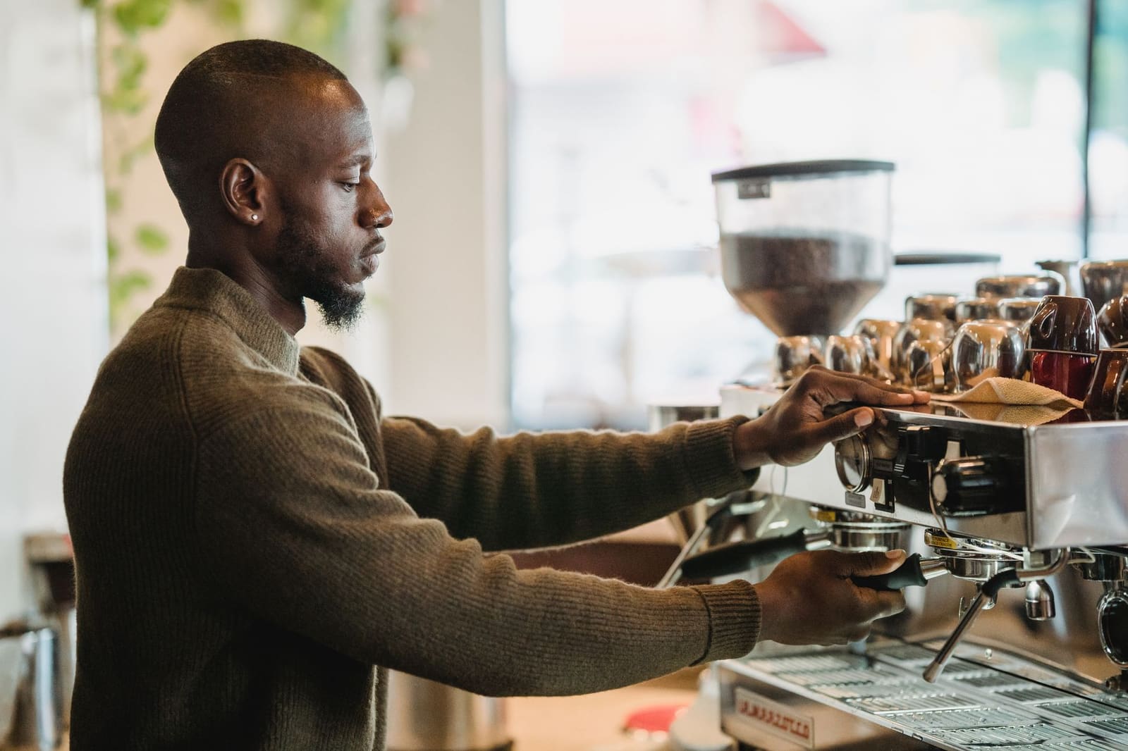 Barista in trui bedient espressomachine in koffiezaak met plant.