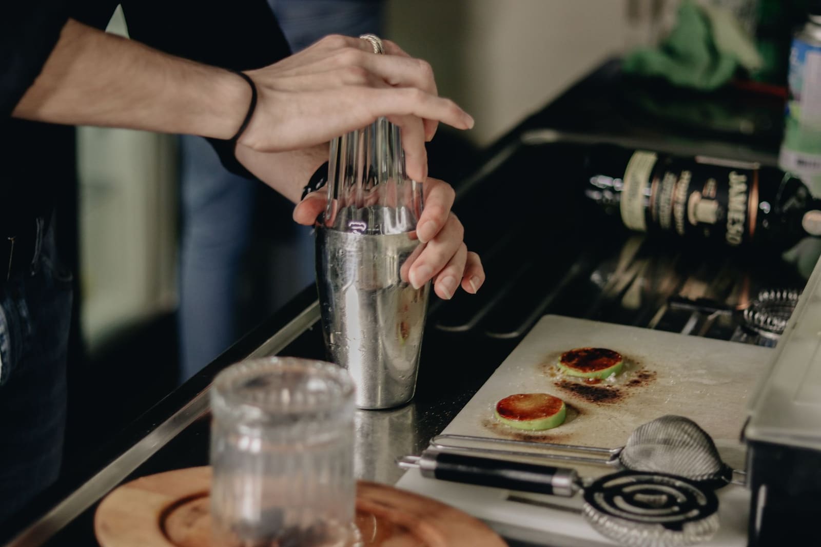 Metalen cocktailshaker en gereedschap klaargezet op een houten bar