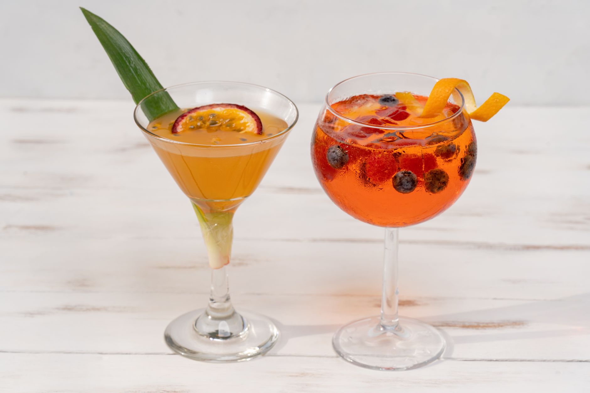 Een spritz met passievruchtlikeur, prosecco en sodawater geserveerd in een wijnglas met ijs en sinaasappelschijf