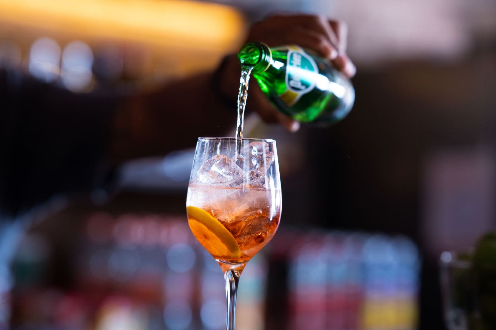 Bartender schenkt frisdrank als mixer in een longdrinkglas met ijs