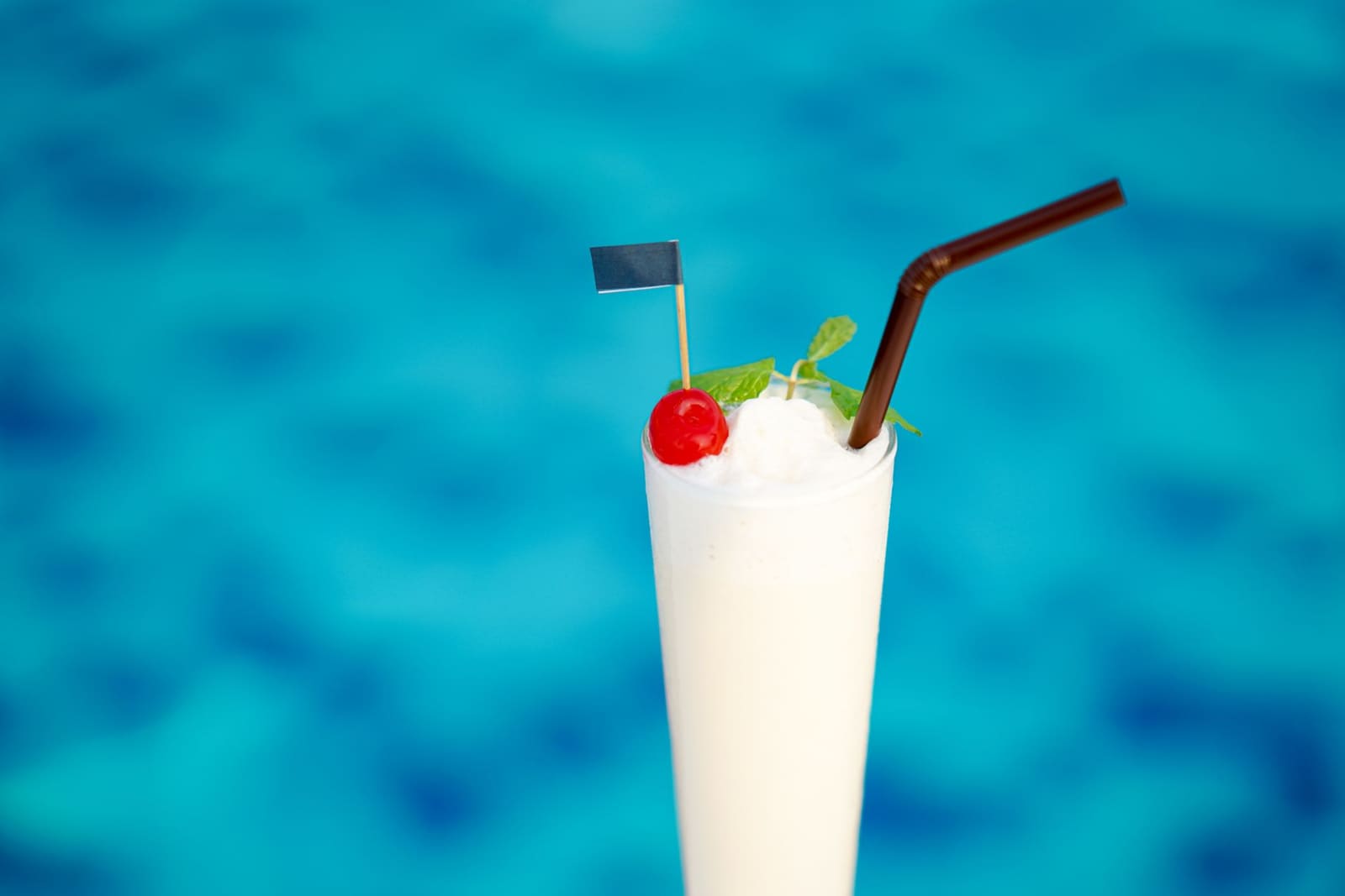 Piña Colada in hoog glas met ananasblad en rietje op een zwembadrand.
