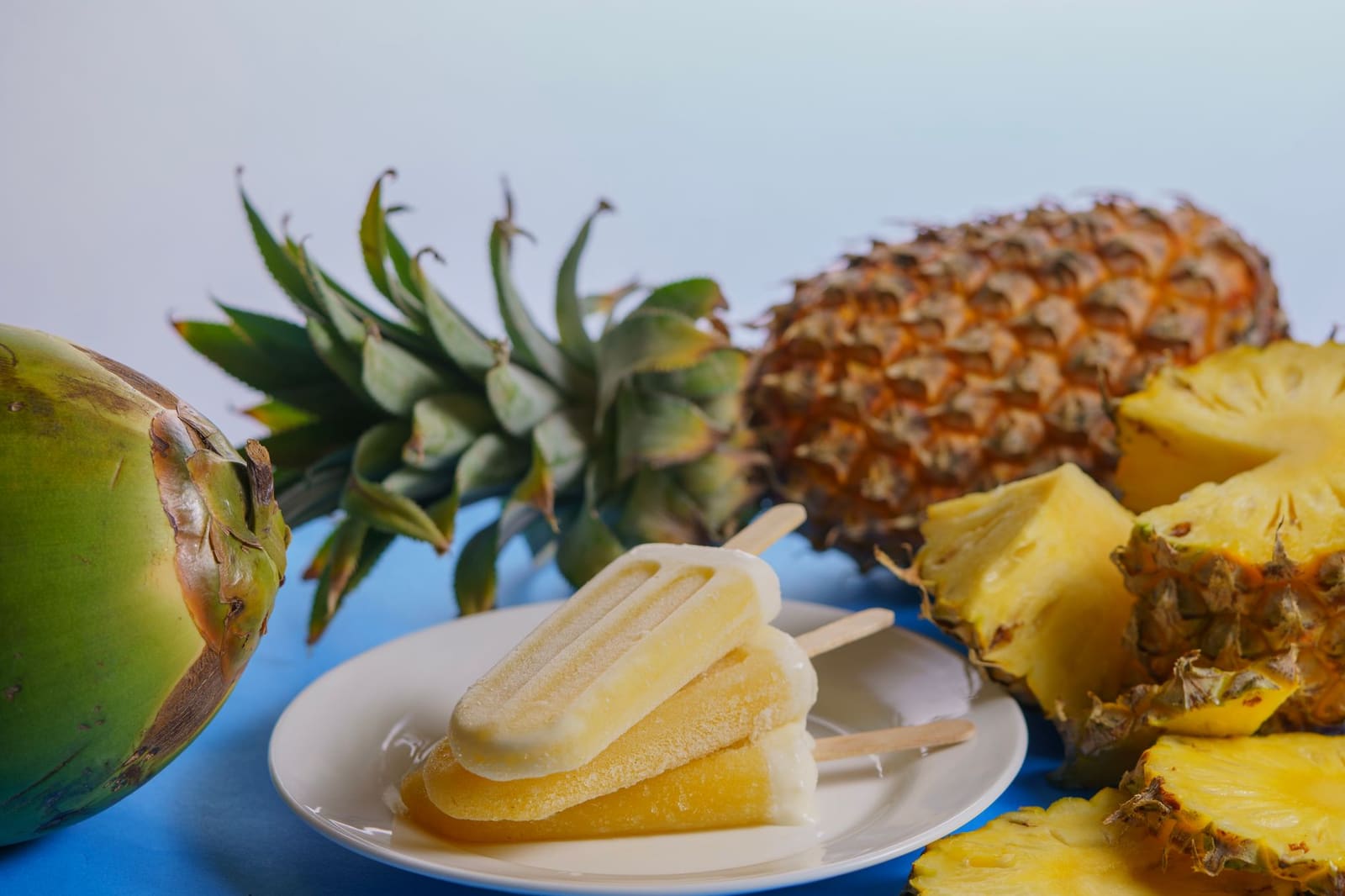 Verse ananas, kokosnoot, limoen en rumflessen liggen klaar op een lichte tafel.