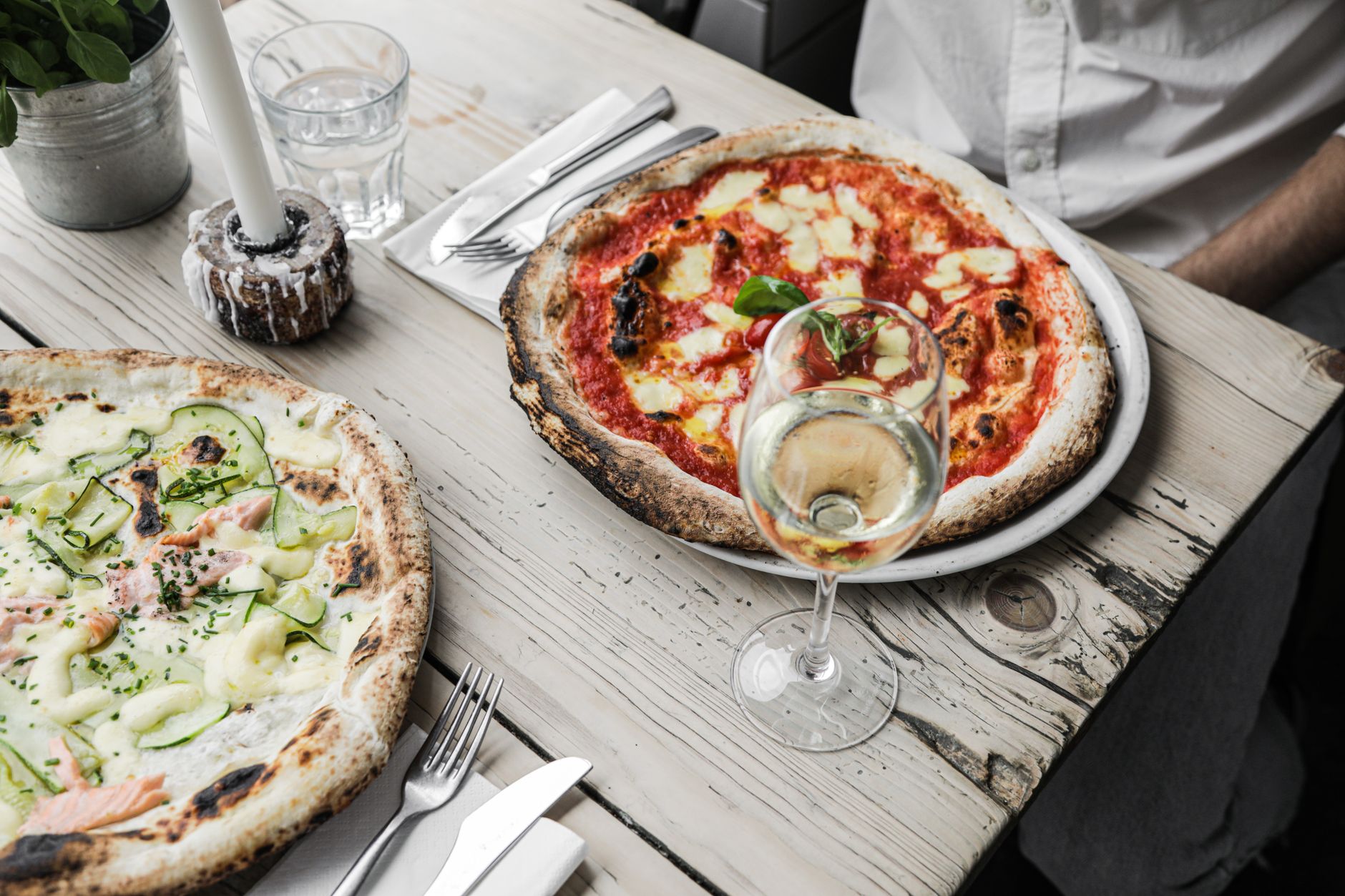 Een glas frisse natuurwijn naast een net gebakken ambachtelijke pizza op een houten tafel