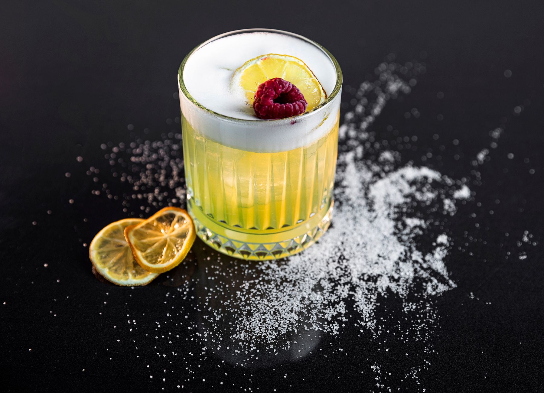 Amaretto Sour cocktail met schuimlaag, sinaasappelschijfje en cocktailkers in rocksglas