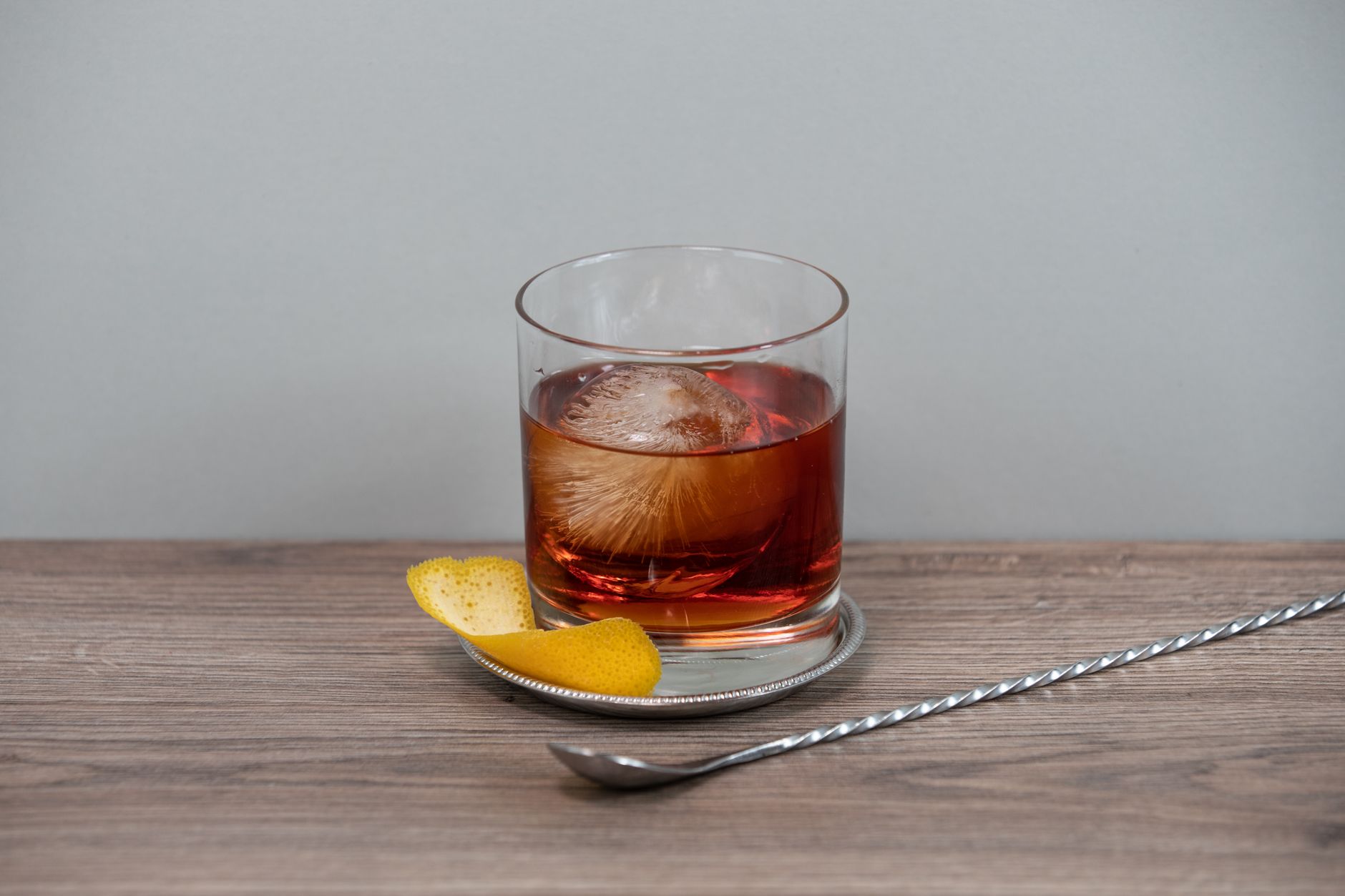 Boulevardier cocktail in rocksglas met groot ijsblok en sinaasappelschil op een houten bar