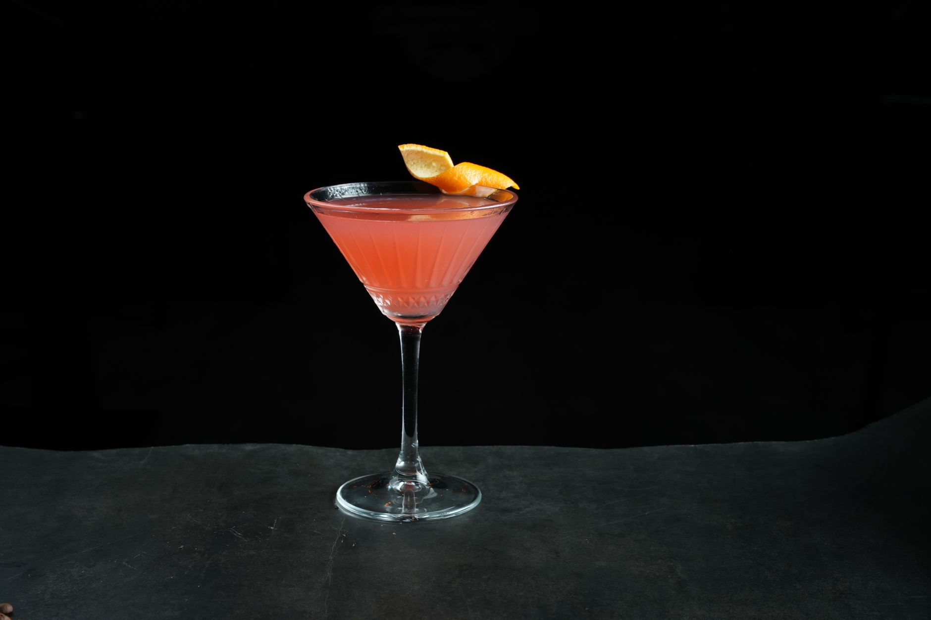 Roze Cosmopolitan cocktail in een coupe glas met sinaasappelschil als garnish