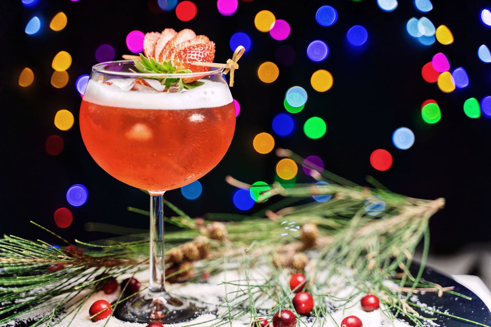 Cranberry Spritz in een groot wijnglas met rozemarijn en limoenschijfje tegen een feestelijke achtergrond