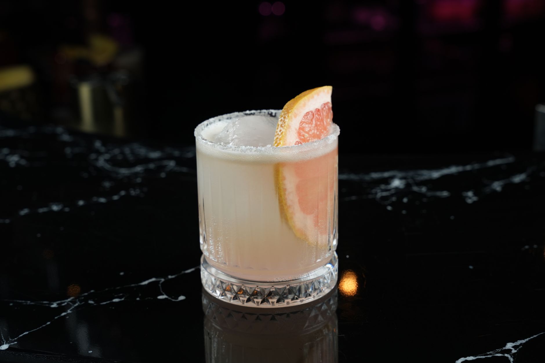 Paloma cocktail in een highballglas met grapefruitpartje en zoutrand op een bar