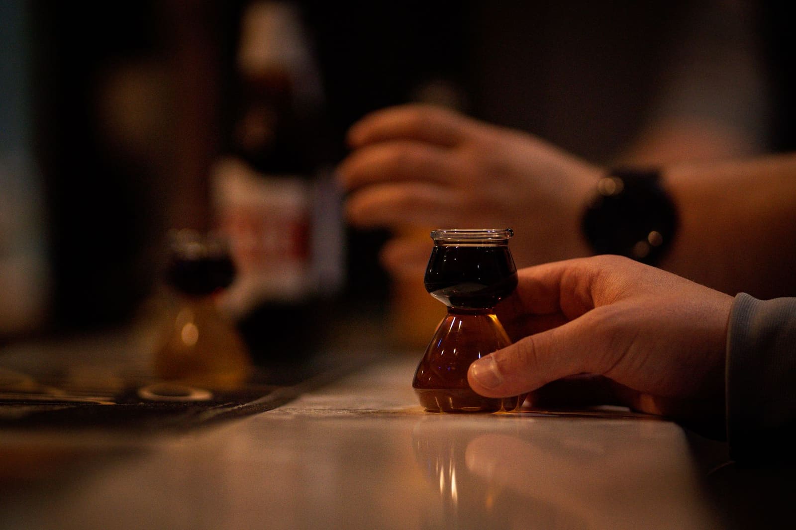Close-up van een hand die een glas amberkleurige whisky vastpakt aan een bar.