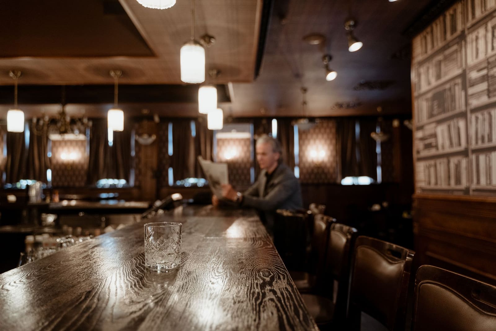 Man leest krant aan oude bar met whiskyglas, sfeervolle verlichting.