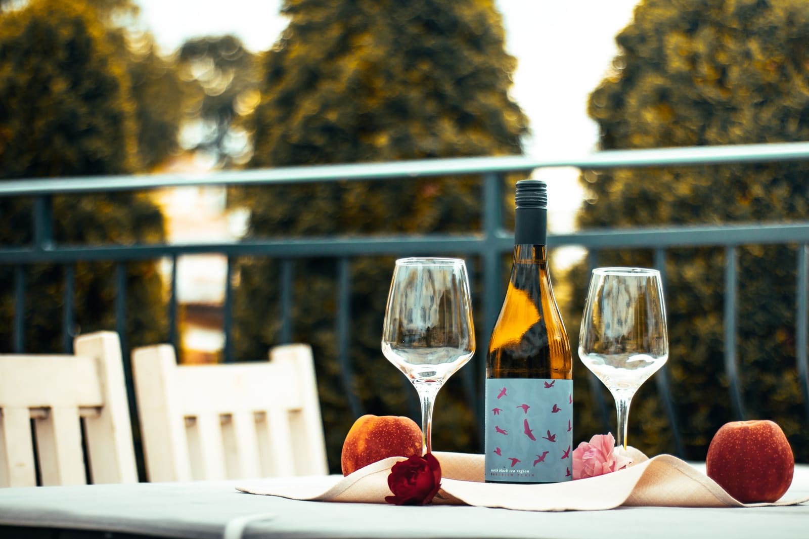 Spritz-achtig tafereel met wijnfles, twee glazen, fruit en bloem op balkon.
