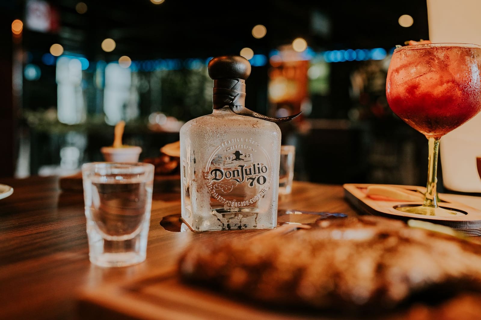Fles tequila op een donkere bar tussen cocktailglazen en citrusfruit