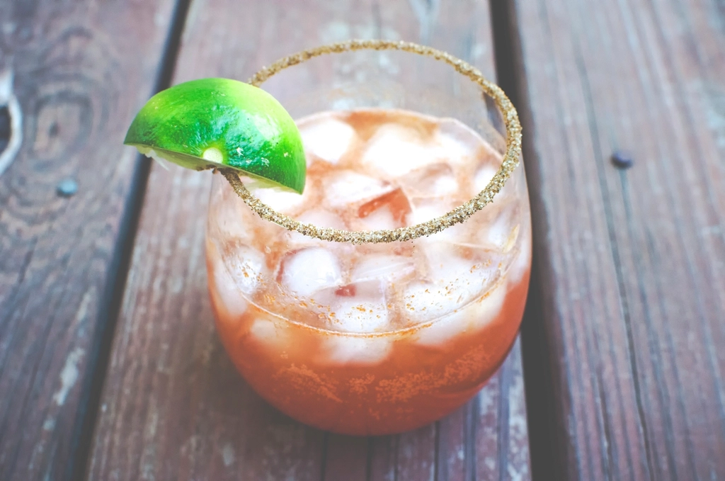 Tomaatcocktail met ijs, limoen en een kruidenrandje in een laag glas