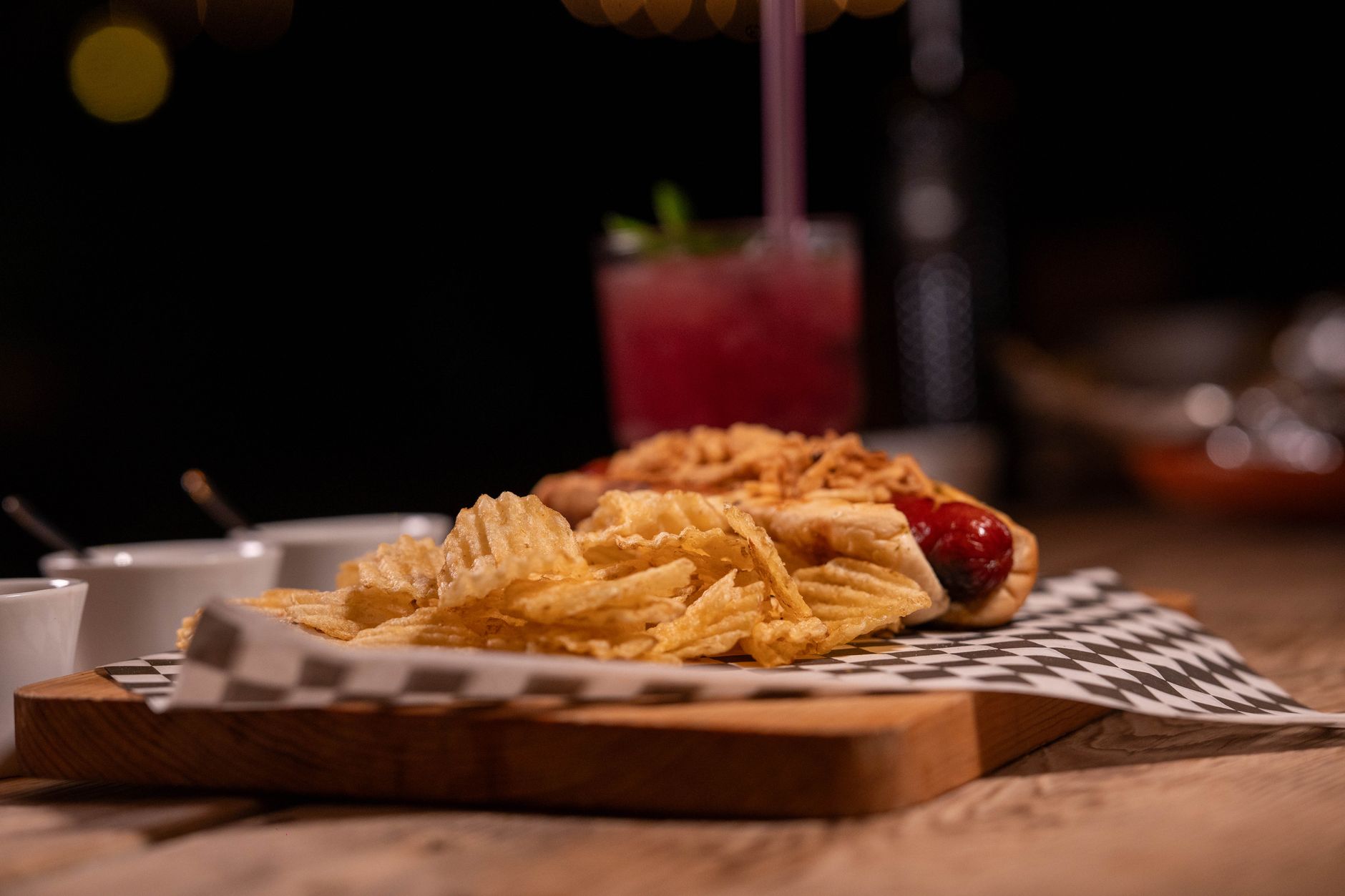 Een gastronomisch belegde hotdog met toppings geserveerd naast een cocktail in een New Yorkse bar