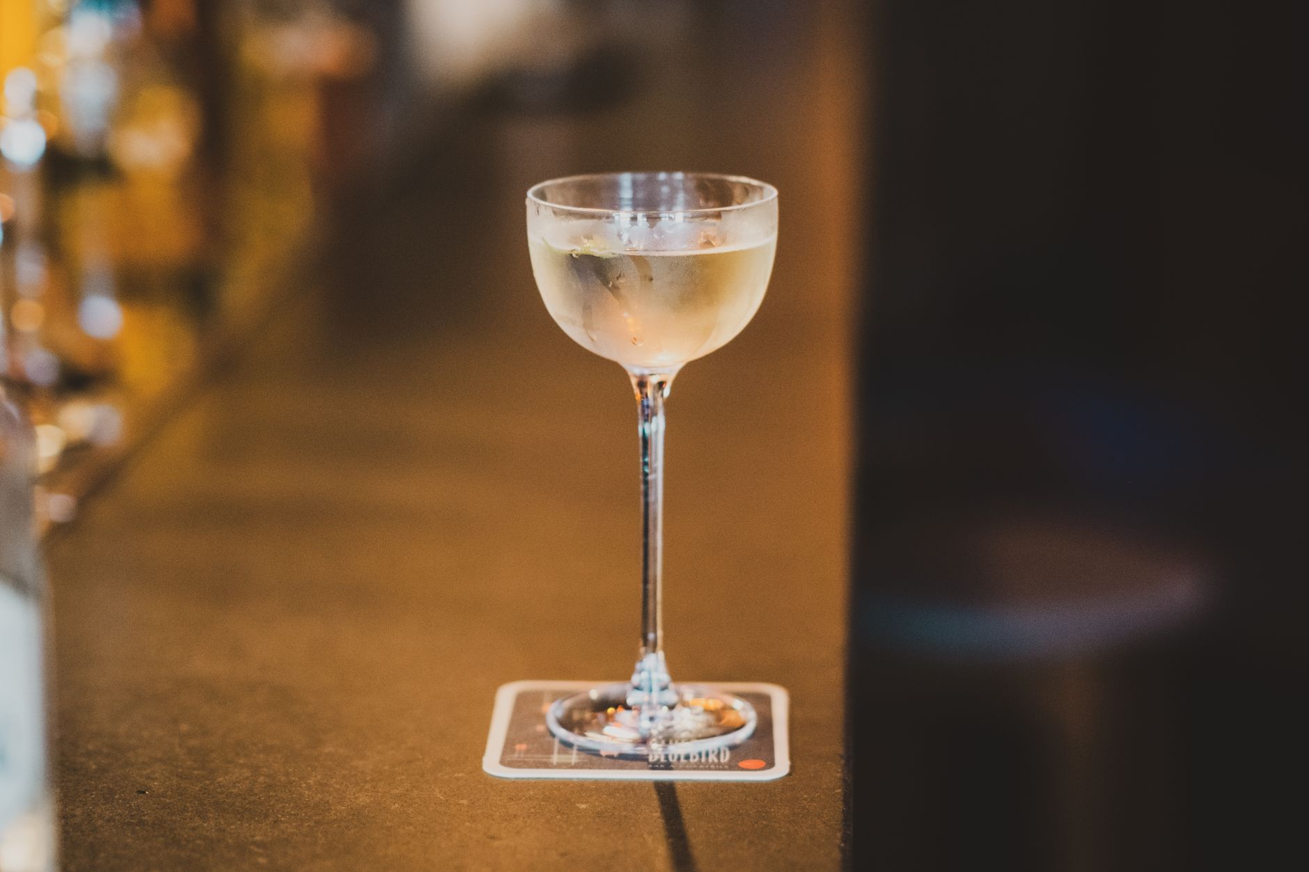 Een heldere Gimlet cocktail met limoen wordt geserveerd achter een drukke bar