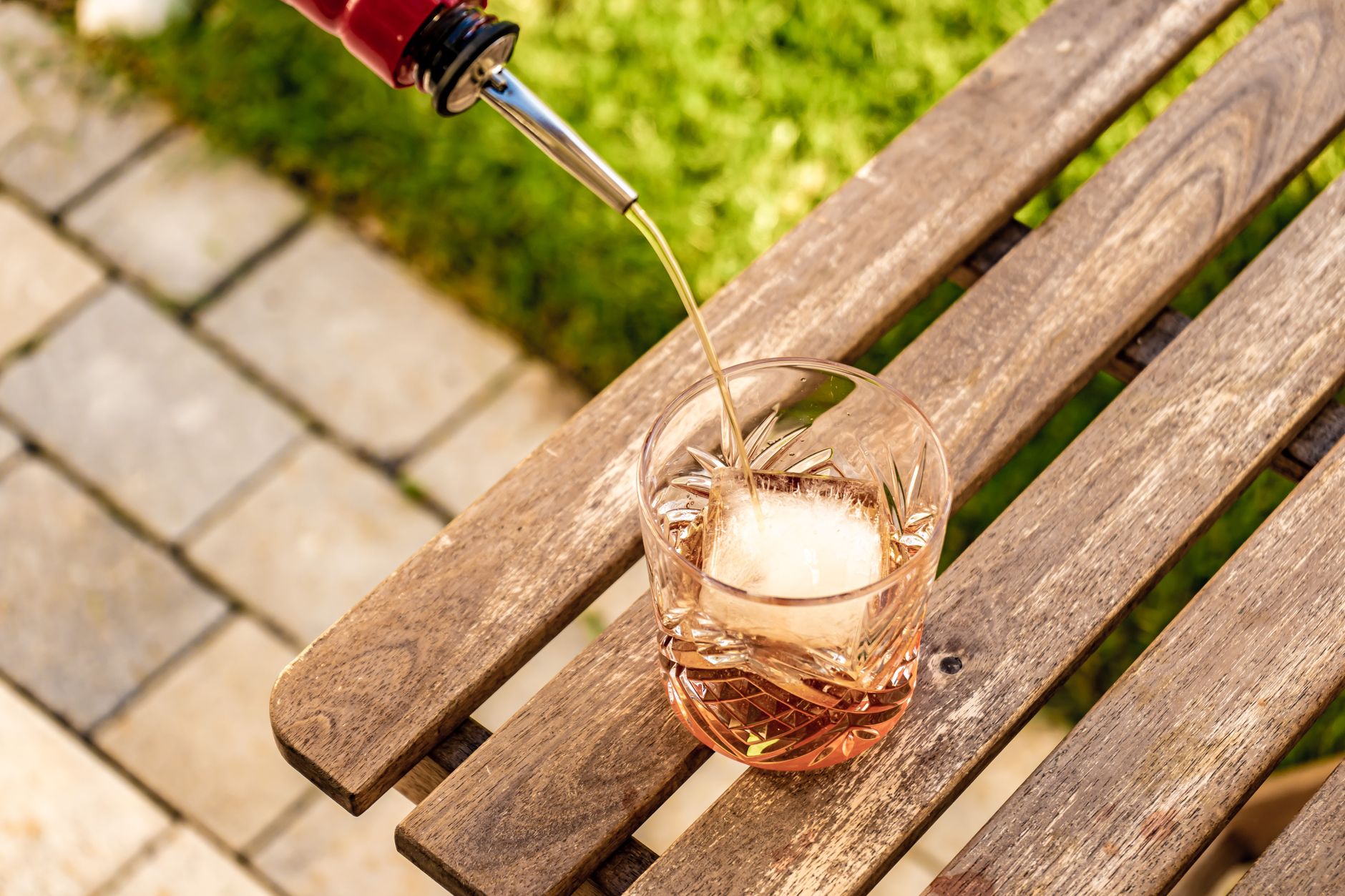 Een kristalhelder, groot ijsblok in een glas met een amberkleurige cocktail achter de bar