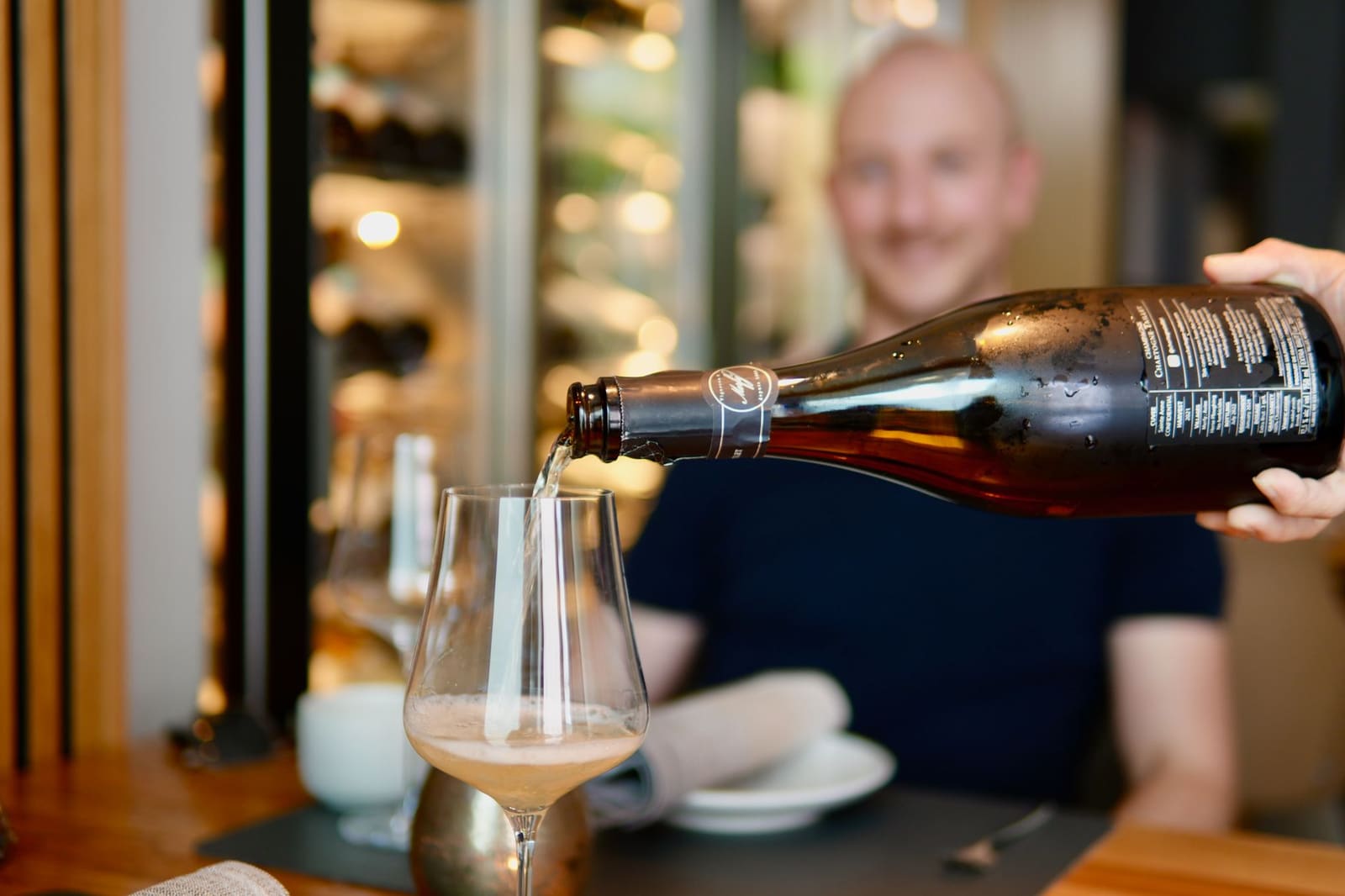 Serveerster schenkt gemberbier of drank in wijnglas voor glimlachende man aan tafel.