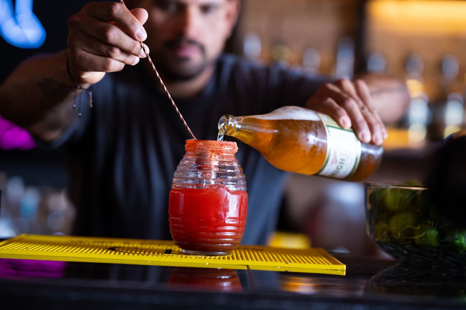 Een barman roert een cocktail in een mixglas met een lange barlepel.
