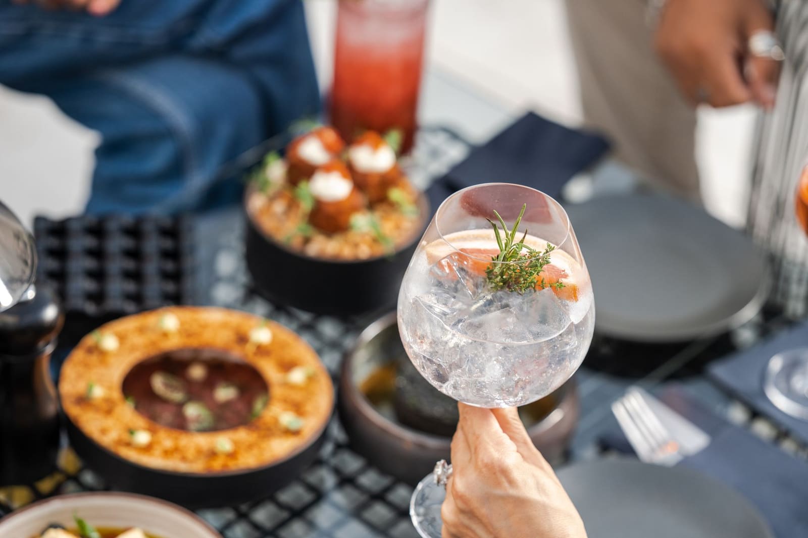 Close-up van een gin-tonic met rozemarijn, bij hapjes op een terrastafel.
