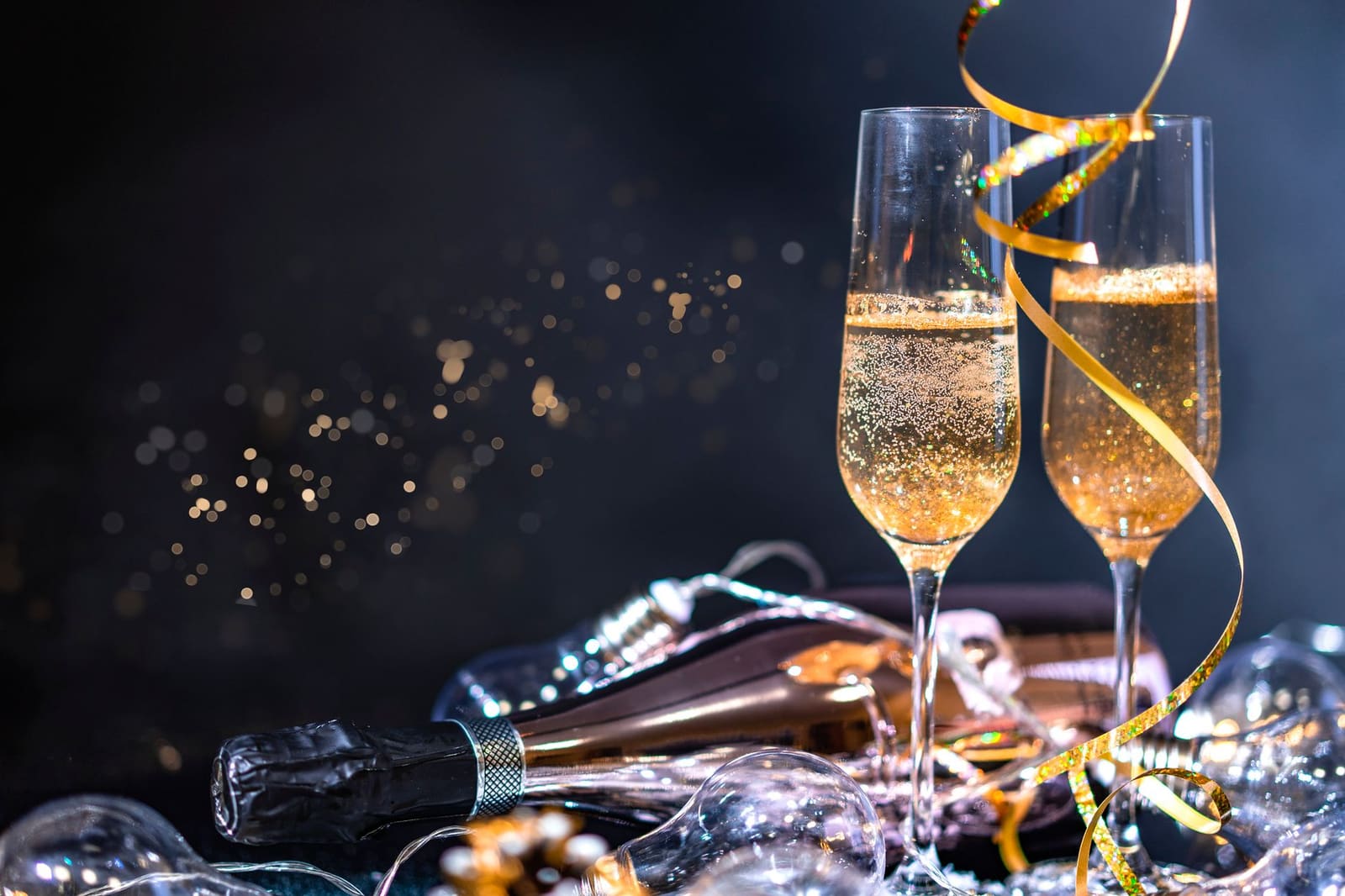 Twee champagneglazen met bubbels, fles en gouden slingers op feestelijke tafel