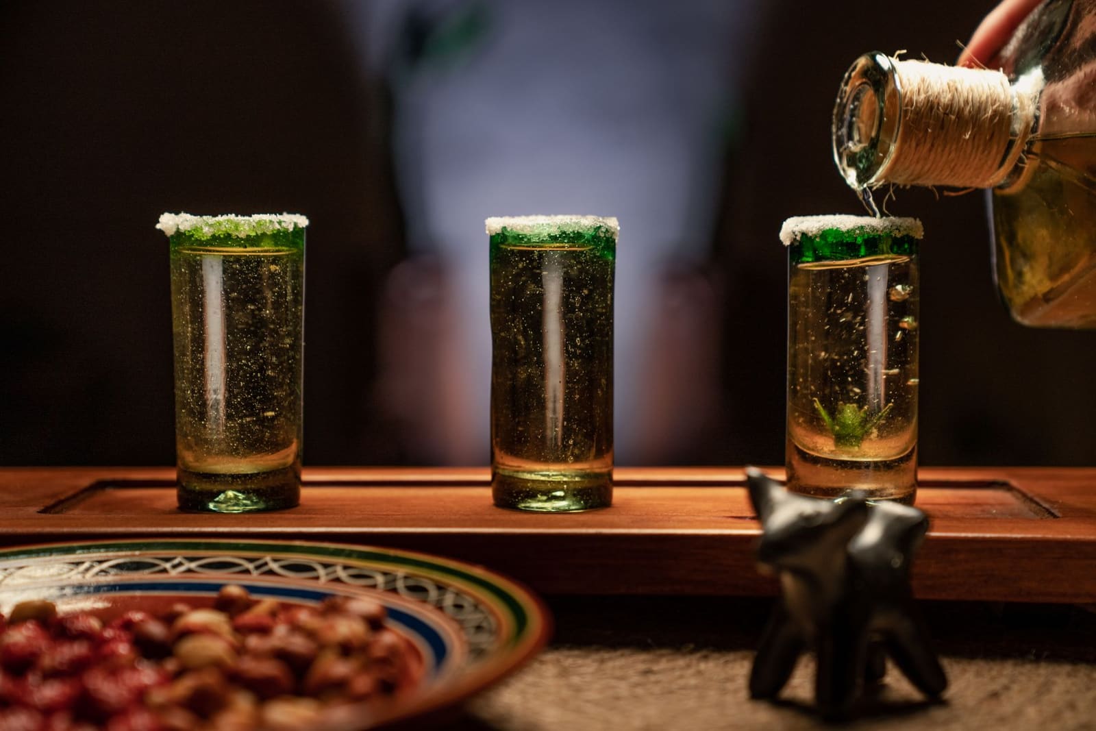 Drie tequila's in kleine glaasjes op een houten plank met een schaaltje limoen.
