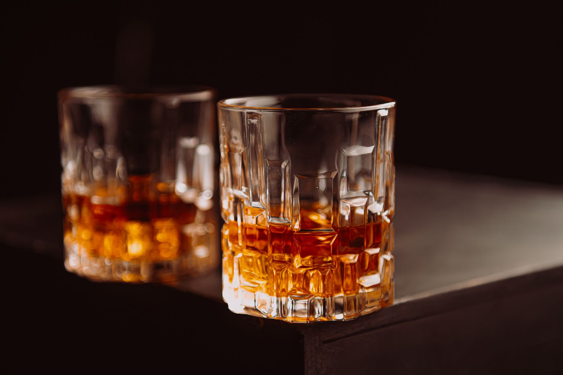 Glas bourbon whiskey met ijsblokje op een houten bar, omringd door flessen
