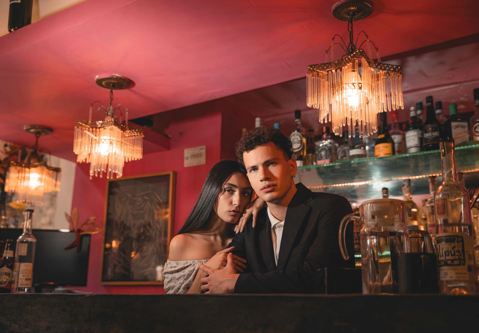 Stel bij de bar knuffelend koppel tussen flessen drank en kroonluchters.