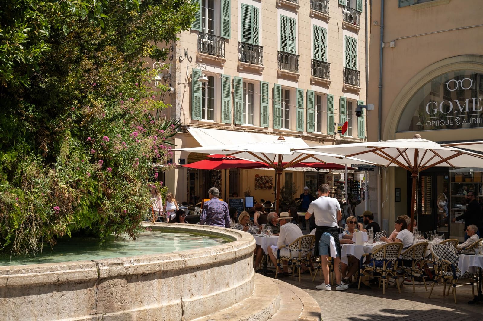 Terrasje in Frankrijk met glazen op tafels bij een fontein en bistrogevel.
