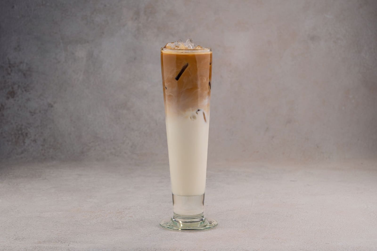 IJskoffie met melk en koffie in gelaagde lagen, hoog glas, grijze achtergrond