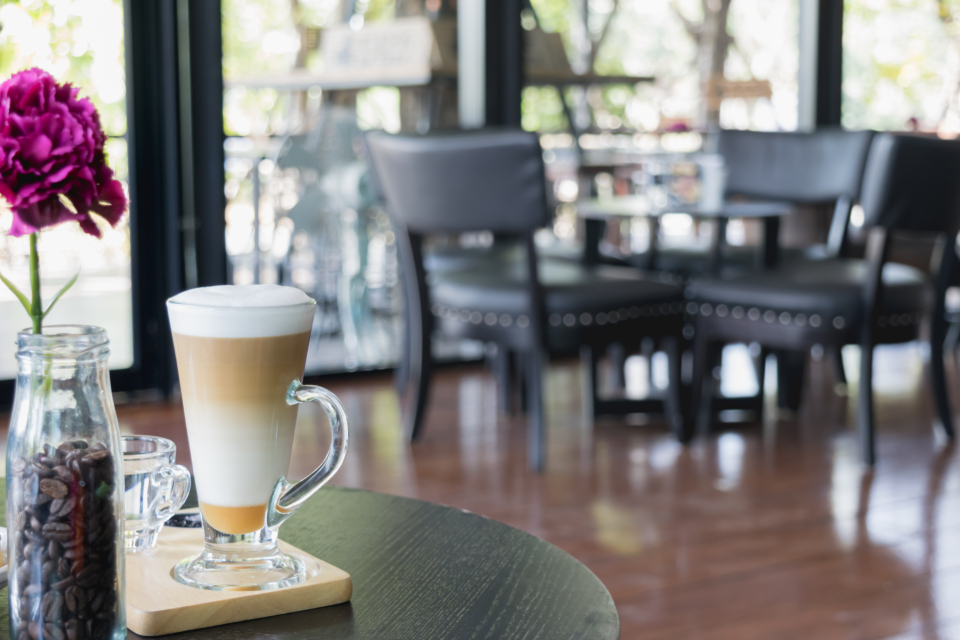 Een latte met kaneel en siroop wordt geserveerd in een glazen kopje op een houten bar