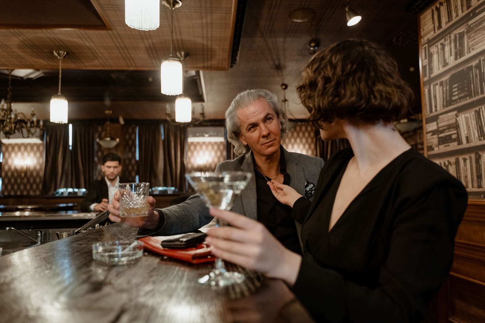 Man en vrouw proosten met martini en whisky aan een barstoel in sfeervolle bar
